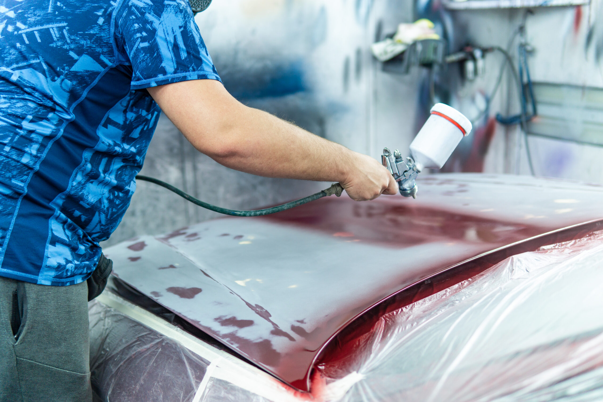Auto mechanic painting a red car in a workshop, copy space